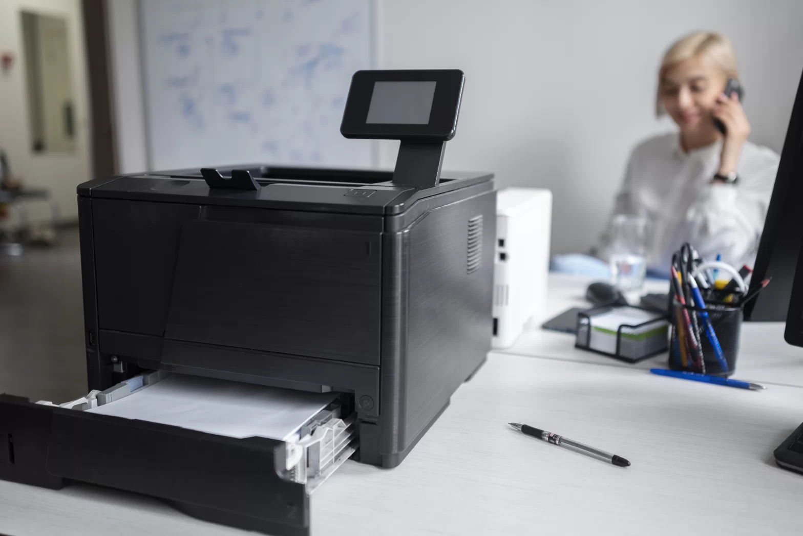 A woman handles a phone call while working near the office printer.