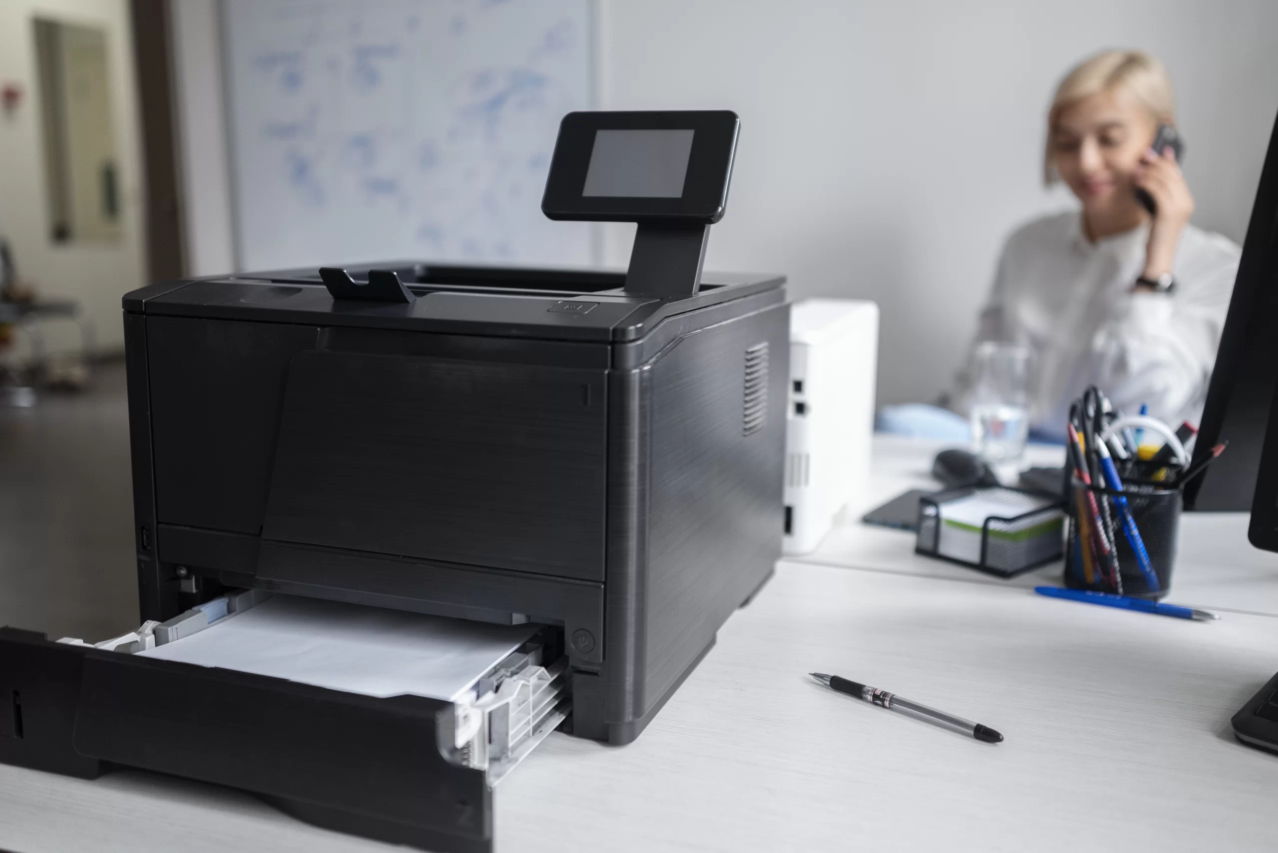 A woman handles a phone call while working near the office printer.