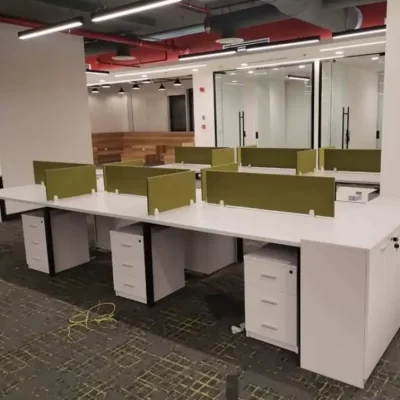 A modern office with long white desks and green partitions, creating individual workspaces