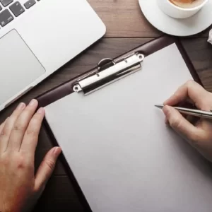 A writing board with a blank sheet of paper, alongside a laptop, a cup of coffee, and a pen.