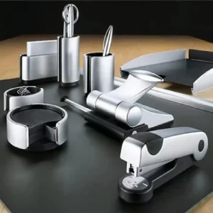 Modern office desk set with various silver and black desk accessories, including a stapler, paper tray, pen holder, and more.