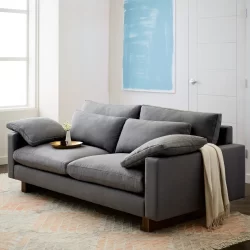 Luxury grey sofa furniture with a cream-colored throw, a flower vase, and a cup on a plate.